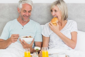 Happy mature couple having breakfast in bed at home